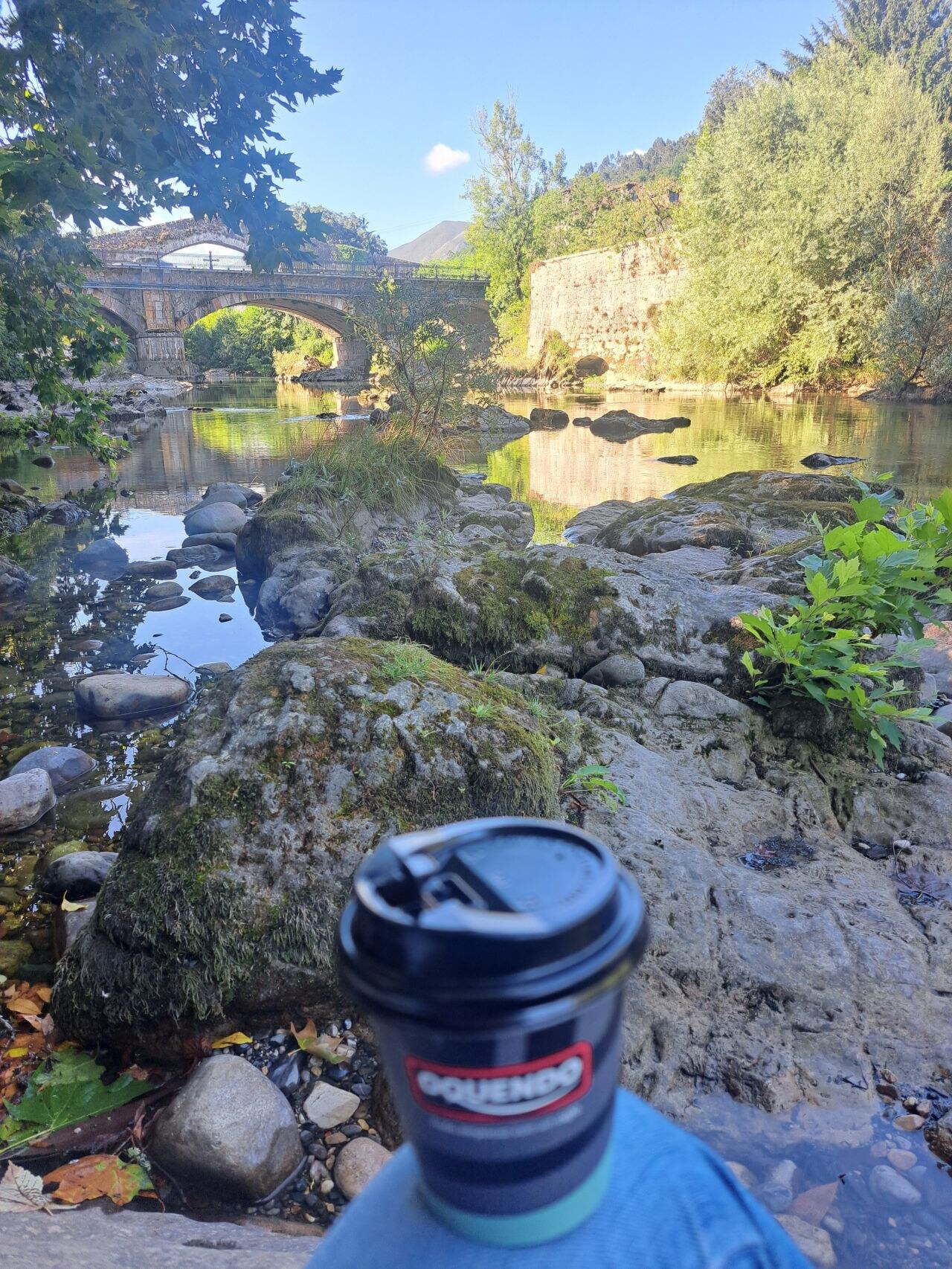 Un café frente al río y un puente de piedra durante un viaje de María Eugenia