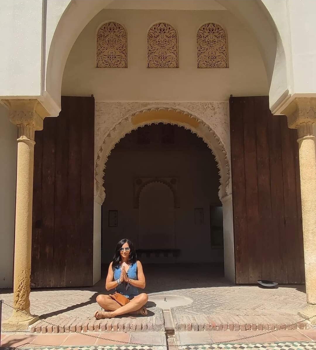 María Eugenia sentada en gesto de namaste ante un patio histórico
